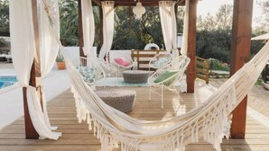 A hammock under a wooden pergola with white curtains, wicker chairs, and a pool in the background. - Oasis in tropical gardens with swimming pool (Moncarapacho)