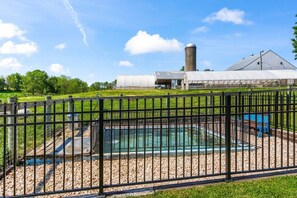 En swimmingpool omgivet af et hegn, med et drivhus og et silo i baggrunden.