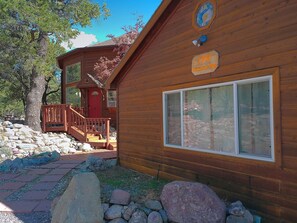 A wooden cabin with a red door, a sign reading '1361 Chapel of Way,' and a large window. - Golden Harmony Cottage (Crestone)