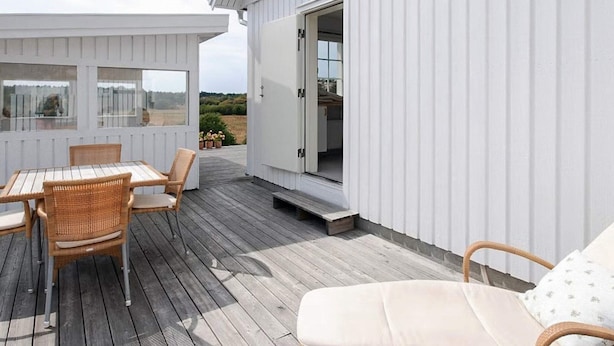 A wooden deck with a table and chairs, a lounge chair, and a white building with a door. - 4 Star Holiday Home in Grebbestad (Grebbestad)