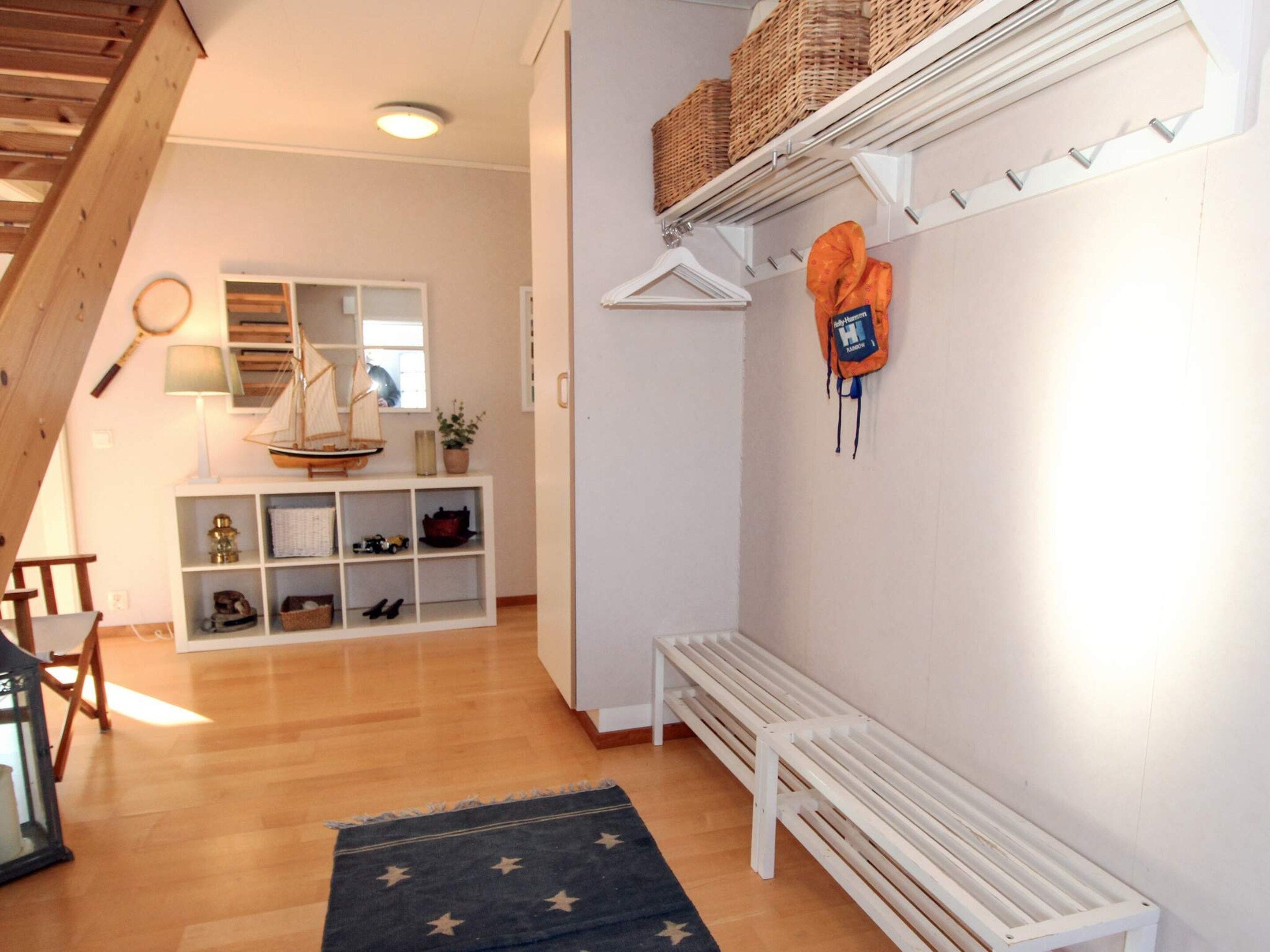 Een kamer met een houten vloer, een bankje, een plank met manden, een hangende tas en een klein model zeilboot.
