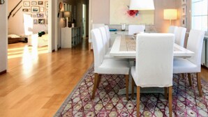A dining area with a white table and chairs, a patterned rug, and a painting on the wall. - 4 Star Holiday Home in Grebbestad (Grebbestad)
