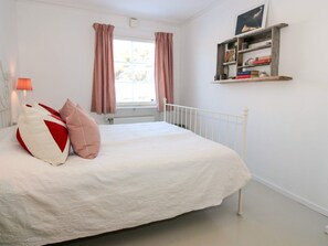 A bedroom with a bed, pillows, a bedside lamp, a window with curtains, and a shelf with books. - 4 Star Holiday Home in Grebbestad (Grebbestad)