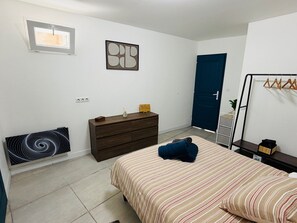 A bedroom with a bed, dresser, radiator, artwork, door, and a coat rack.