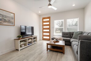 Una sala de estar con televisor, sofá, mesa de centro y una puerta de madera con persianas.