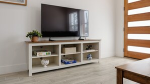 Un televisore a schermo piatto su un'unità porta TV bianca con ripiani, una pianta e oggetti decorativi.