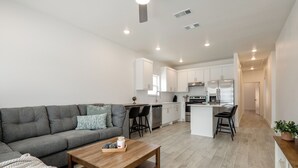 Un appartamento moderno con divano grigio, tavolino in legno, cucina bianca e una piccola isola.