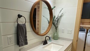 A bathroom with a double sink, a mirror, a towel rack, a toilet paper holder, and a green plant.