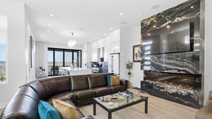 A modern living room with a leather sofa, a glass coffee table, a fireplace, and a large TV mounted on a marble wall. - Luxury Mt Adams Retreat Suites (Cincinnati)