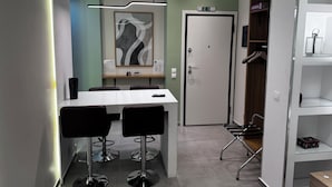 Ett modernt matområde med ett vitt bord, svarta stolar, ett inramat abstrakt konstverk och en dörr med en skylt ovanför.