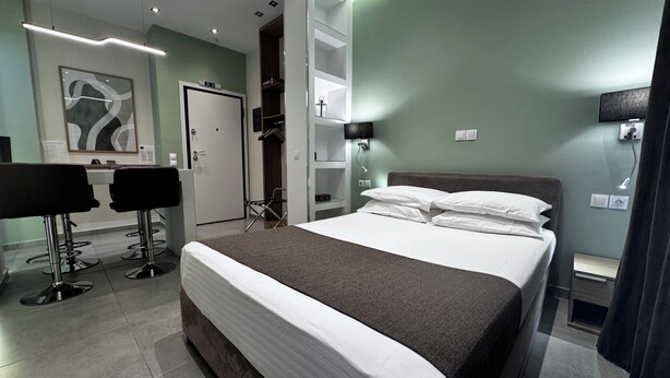 Ett modernt hotellrum med en stor säng, ett skrivbord med två stolar, en garderob och en spegel.