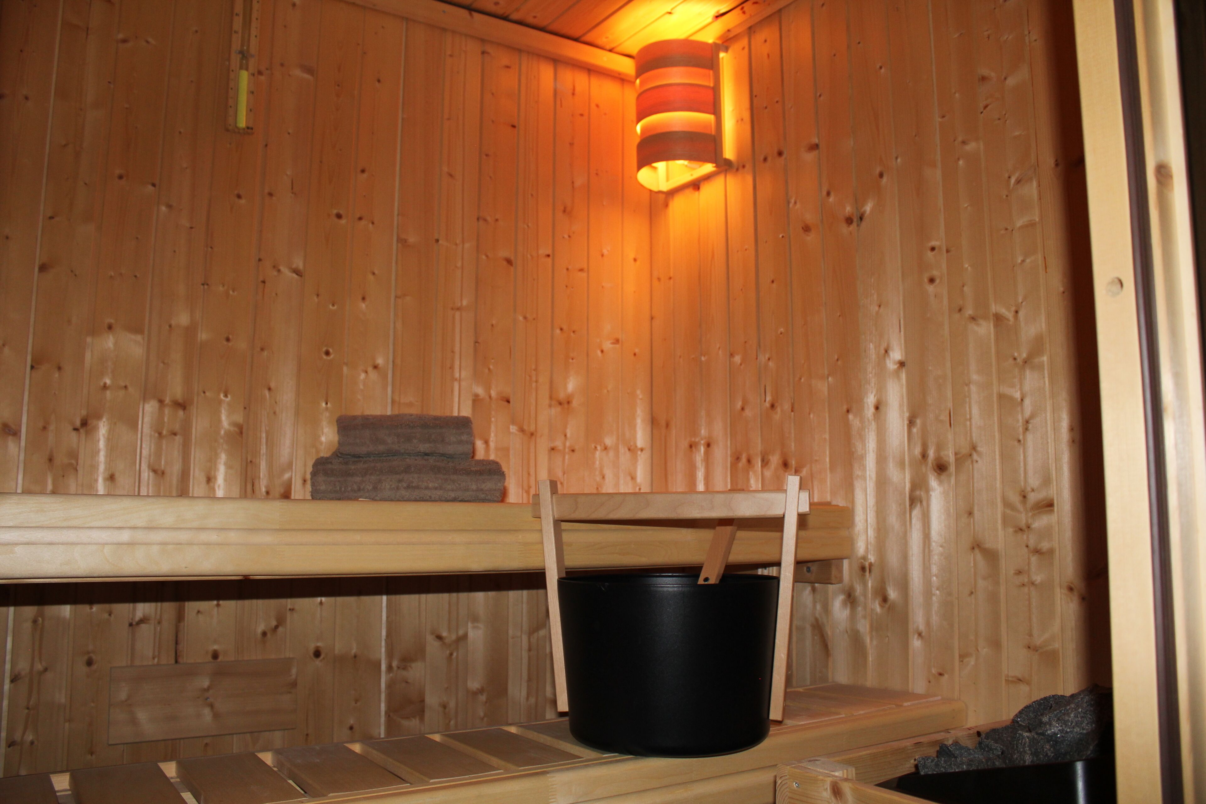 Eine Holzsauna mit einer Sitzbank, einem Eimer und einem Handtuch.