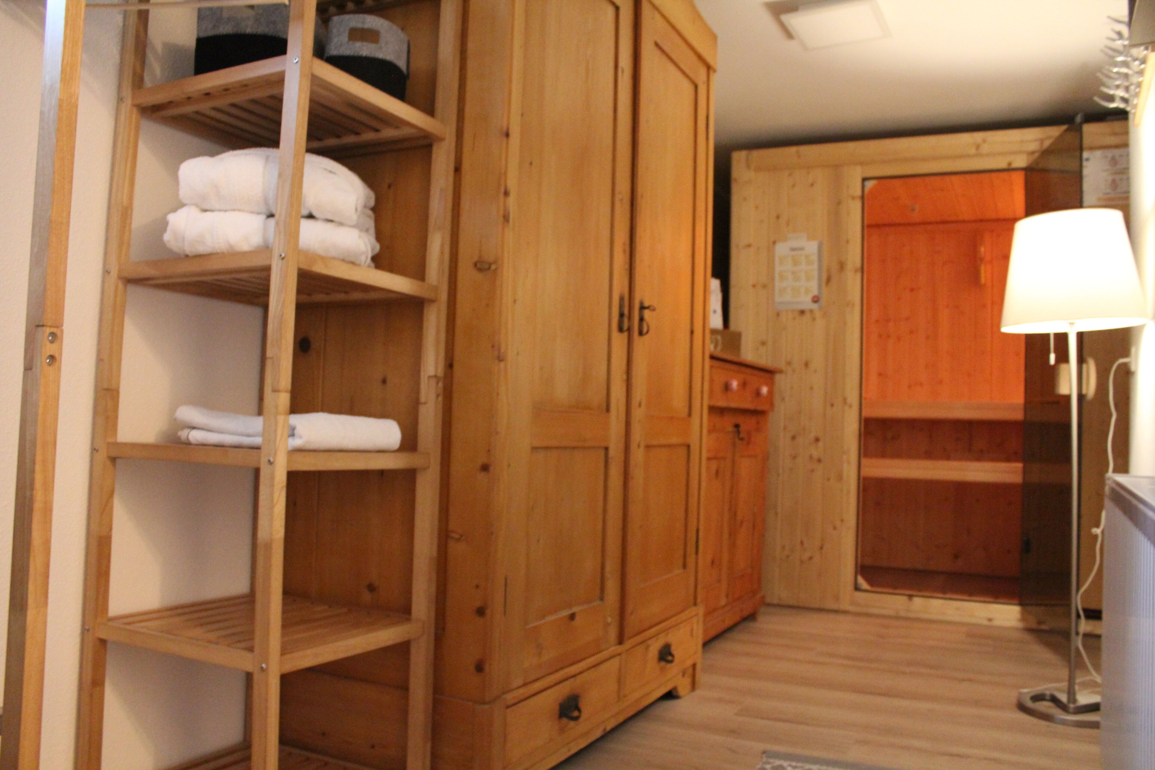 Een houten garderobe met meerdere planken en lades, een houten kastje met een deur, en een lamp aan de rechterkant.