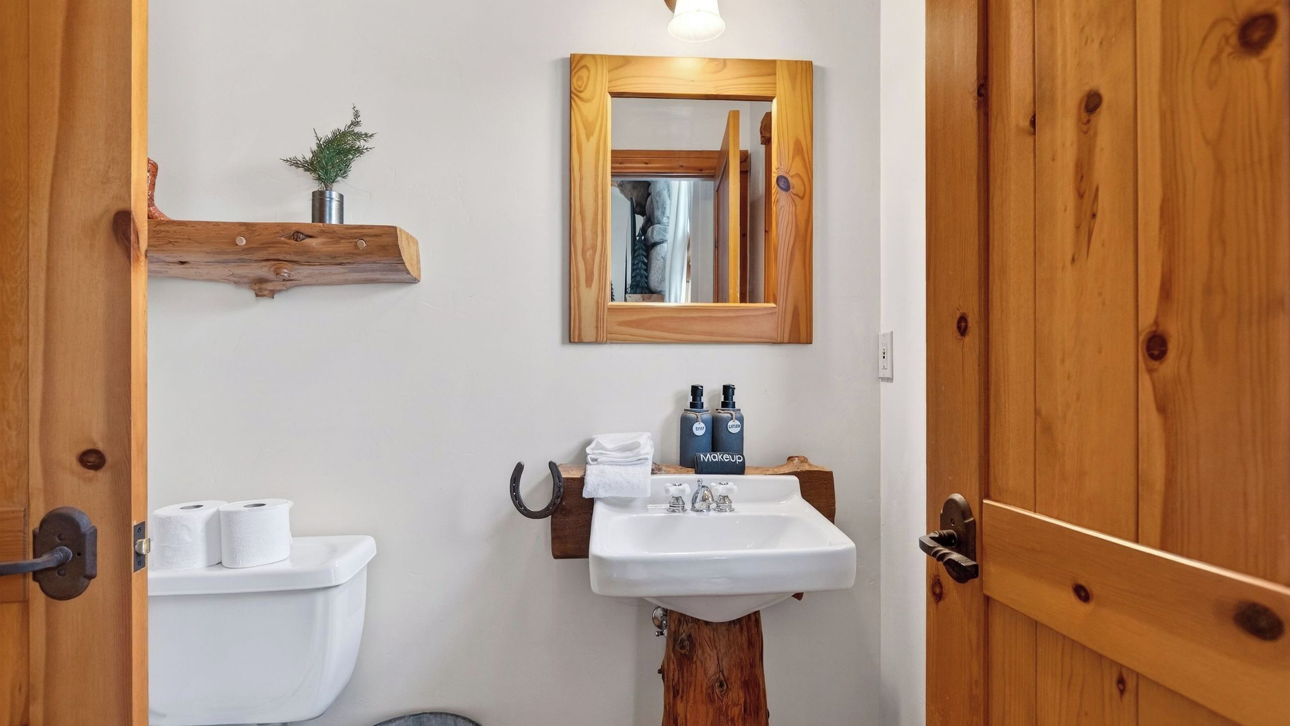 Un baño con puerta de madera, un lavamanos blanco, un espejo y un estante con artículos de aseo.