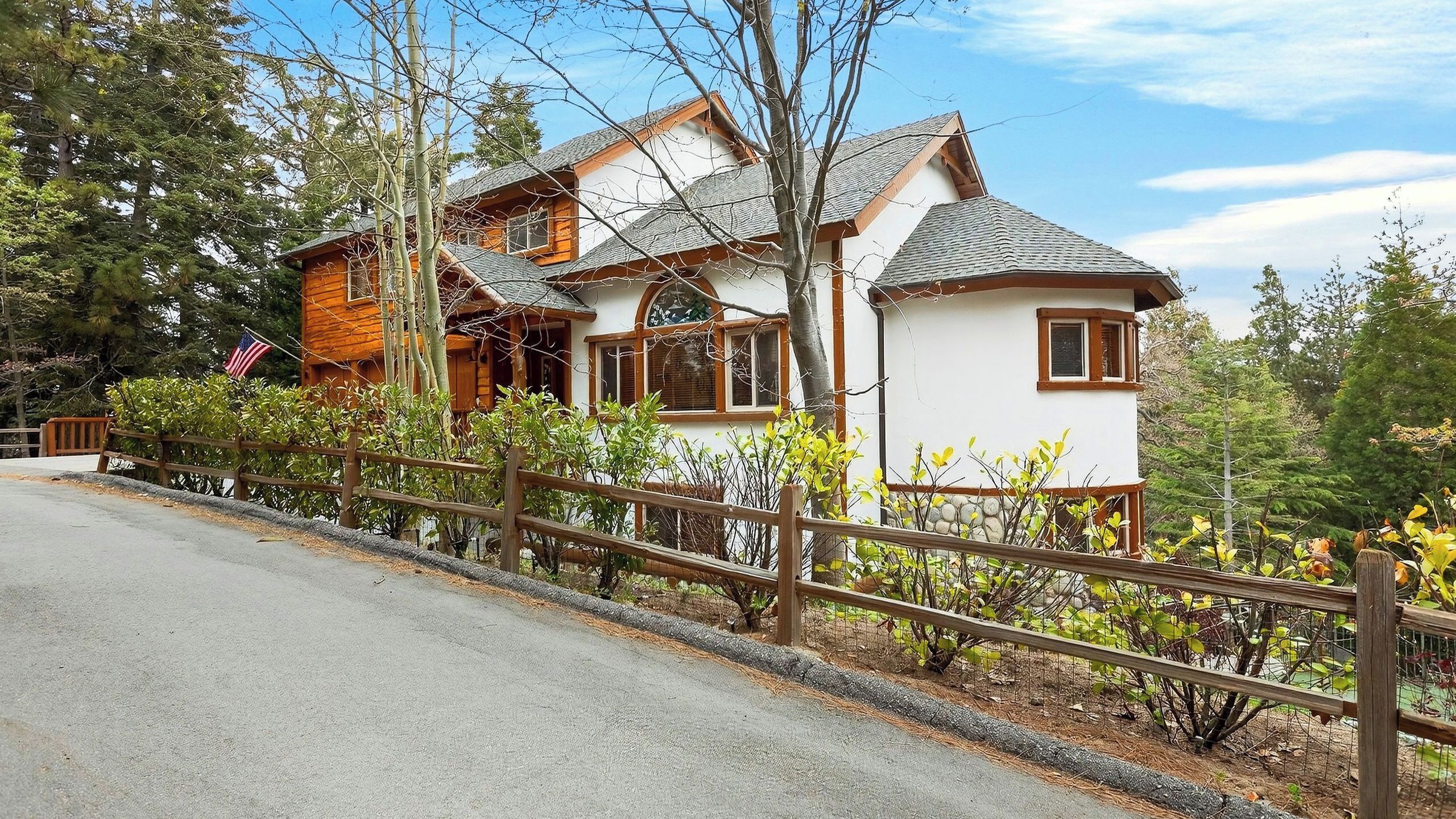 Une cabane en rondins à deux étages, avec une façade blanche, une terrasse en bois et une cour clôturée.