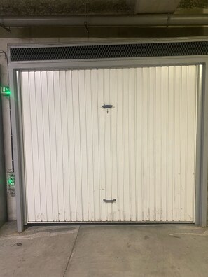 Eine große, geschlossene Garagentür mit einem Metallgitter oben, einem grünen Notausgangsschild und einem Schlüsselloch.