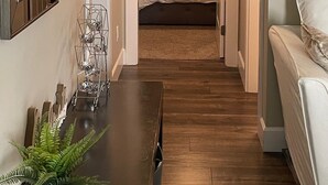 Un pasillo estrecho que conduce a un dormitorio con una cama, una mesita de noche con una planta y un espejo en la pared izquierda.