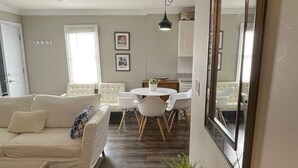 Una sala de estar con un sofá, una mesa de comedor con sillas, una consola negra con una planta y un espejo grande en la pared.