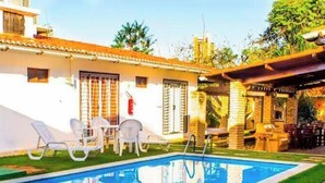 Un espace aménagé au bord de la piscine, avec un bâtiment blanc, une piscine et des sièges extérieurs.