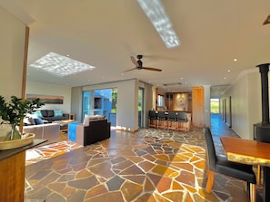 A spacious living area with a stone-tiled floor, a ceiling fan, a bar area, and a kitchen visible through an open door.