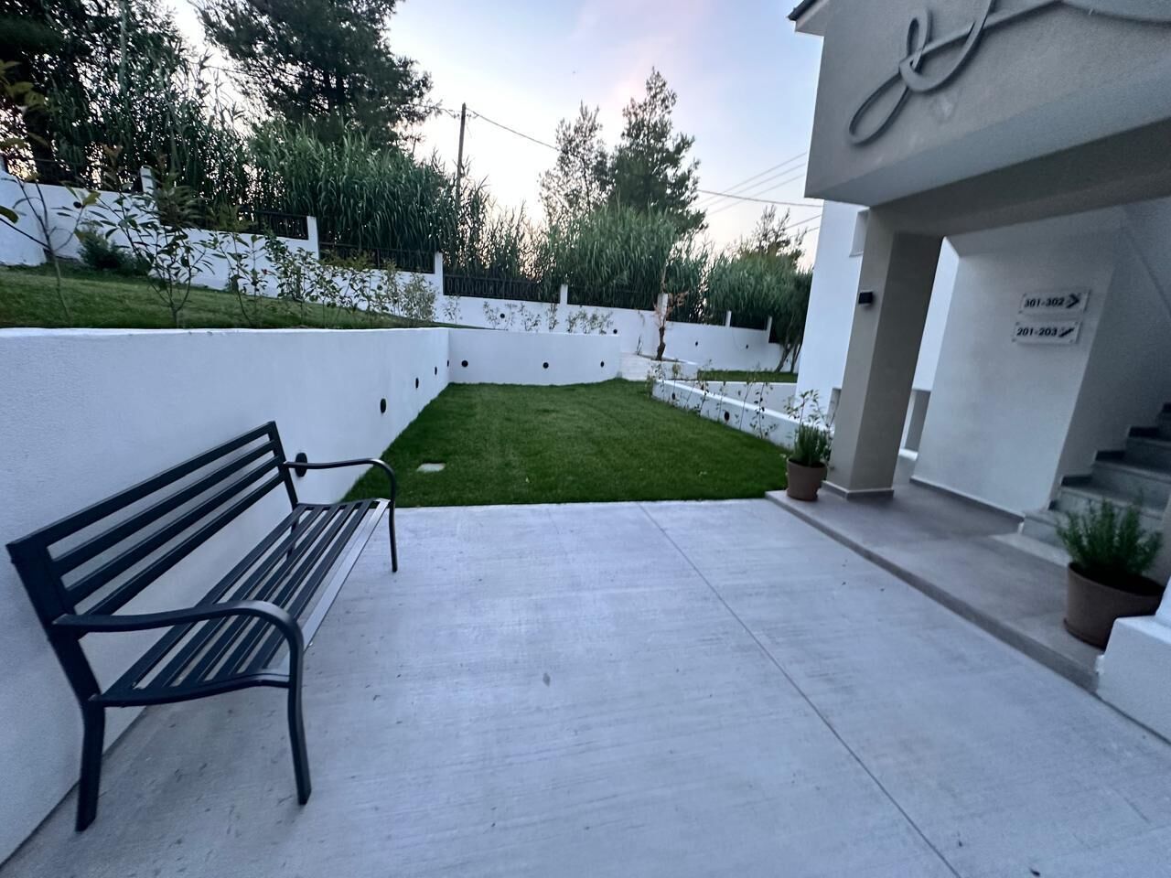 A bench, a small grassy area, and a white wall with a sign.