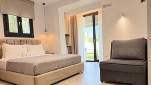 A bedroom with a bed, a chair, a window with curtains, a door, and a 'No Smoking' sign. - MALKA PREMIUM SUITES (Kassandra)