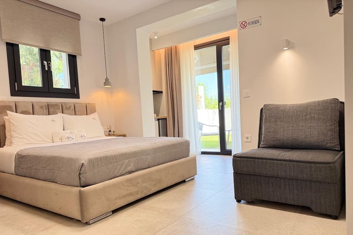 A bedroom with a bed, a chair, a window with curtains, a door, and a 'No Smoking' sign.