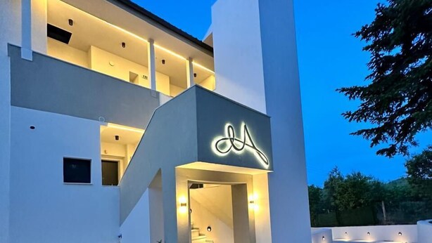 A modern two-story building with a prominent illuminated sign, a staircase leading to the entrance, and a well-maintained lawn. - MALKA PREMIUM SUITES (Kassandra)