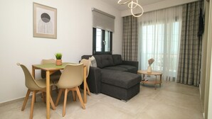 A modern living room with a sofa, dining table, chairs, a small side table, and a pendant light. - MALKA PREMIUM SUITES (Kassandra)