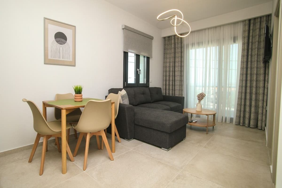 A modern living room with a sofa, dining table, chairs, a small side table, and a pendant light.