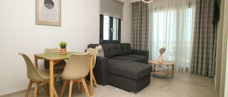A modern living room with a sofa, dining table, chairs, a small side table, and a pendant light.