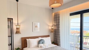 A hotel room with a bed, bedside tables, a hanging light fixture, a framed picture, and a view through a window. - MALKA PREMIUM SUITES (Kassandra)