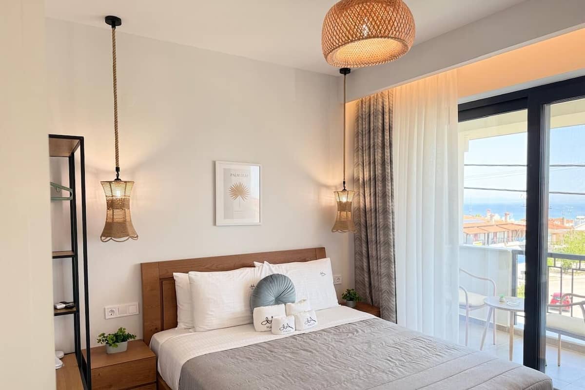 A hotel room with a bed, bedside tables, a hanging light fixture, a framed picture, and a view through a window.