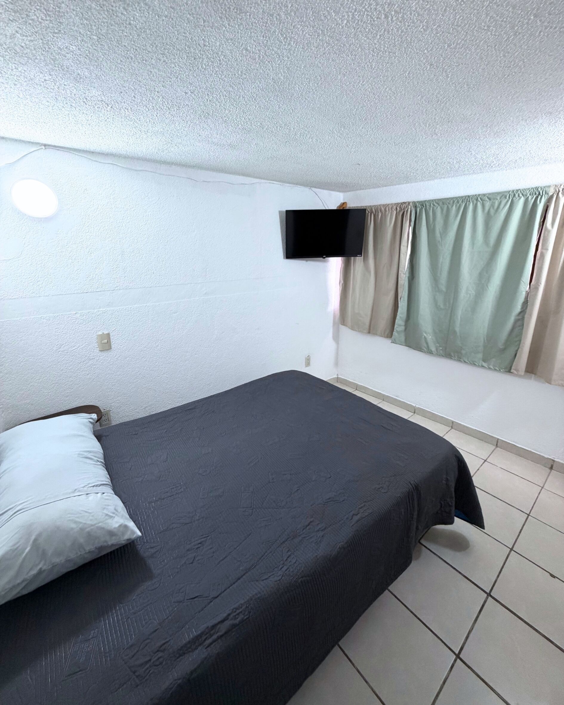 A simple room with a bed, a television mounted on the wall, and a window with curtains.
