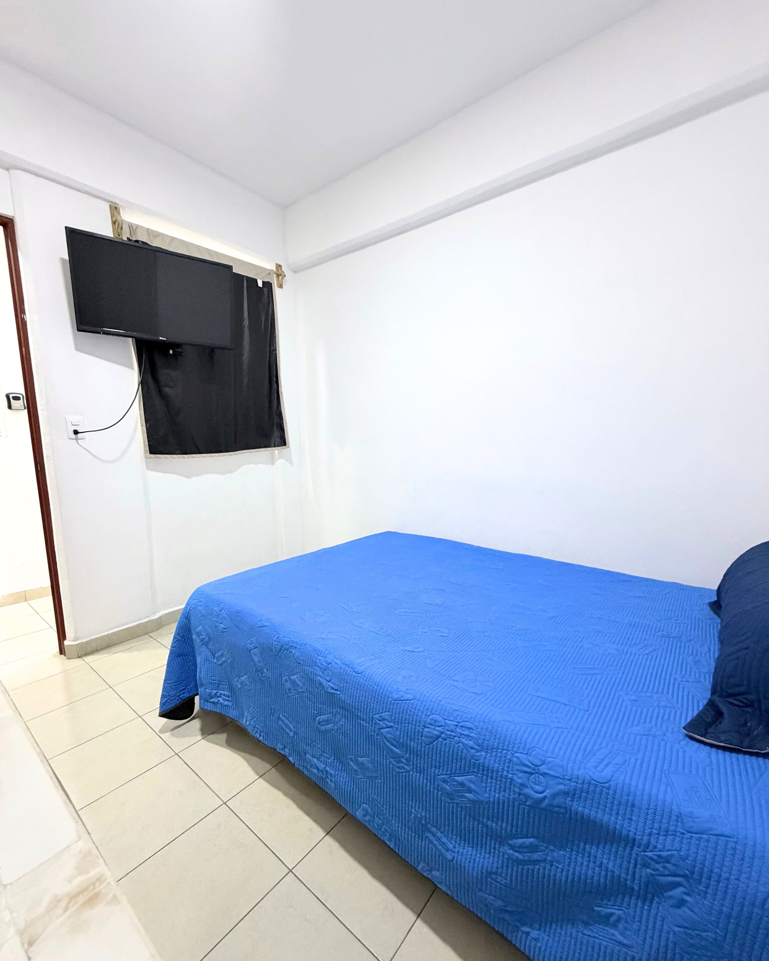 Une pièce avec un lit, un téléviseur fixé au mur et une porte.