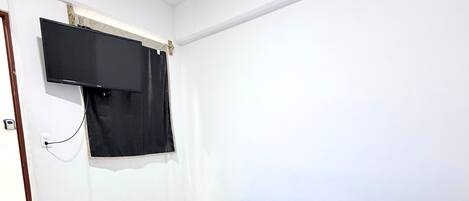 Une pièce avec un lit, un téléviseur fixé au mur et une porte.