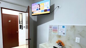 Habitación de hotel con un televisor montado en la pared, encimera de mármol, puerta con un número y suelo de baldosas.