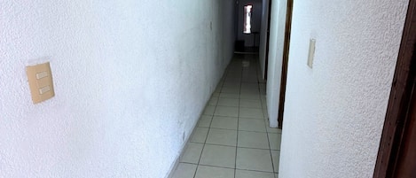 Un pasillo estrecho con paredes blancas y piso de baldosas que conduce a una puerta al final.