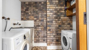 A laundry room with two washing machines, a tiled wall, and a wooden shelf. - Azure - A comfortable holiday unit designed for rest, relaxation, and convenience (South West Rocks)