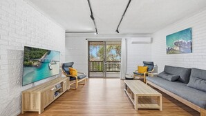 Ein modernes Wohnzimmer mit Fernseher, Sofa, Sesseln und einem Holztisch.