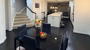 A modern kitchen with white cabinets, a central island, and a dining area with a black table and chairs.
