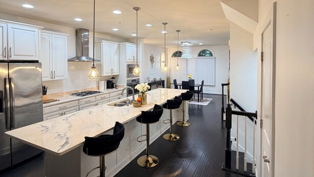 A modern kitchen with a central island, bar stools, stainless steel appliances, and pendant lighting.