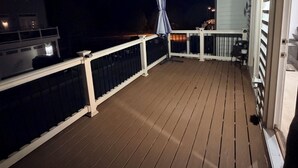 A wooden deck with white railings, a covered seating area, and a building with a lighted entrance.