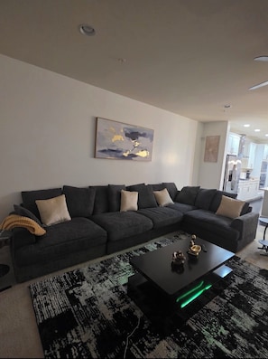 A modern living room with a sectional sofa, a coffee table, and a rug. - Premium Modern Luxe Retreat Near BWI & Arundel Mills (Severn)