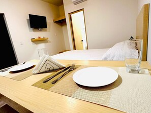 A hotel room with a neatly arranged dining table, a bed with a white comforter, a television mounted on the wall, and a wooden shelf with a small item on it. - APARTMENT 5 CABOLIRA IN SAN JOSE DEL CABO, 15 MIN FROM THE BEACH (San José del Cabo)