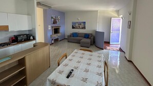 Een knus leefruimte met een kitchenette, een eettafel, een bank en een open haard.