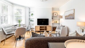 Ein modernes Wohnzimmer mit Fernseher, einer Couch, Sesseln und einem Essbereich mit Tisch und Stühlen.