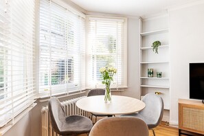 A modern room with a round table, grey chairs, a radiator, white shelves, and a TV. - Stylish Fulham Apartment with Private Garden (London)