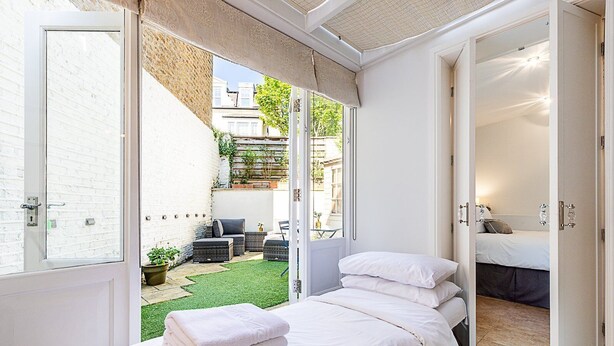 Ein Schlafzimmer mit einem Bett, einer kleinen Sitzecke mit Tisch und Stühlen sowie Blick ins Freie.