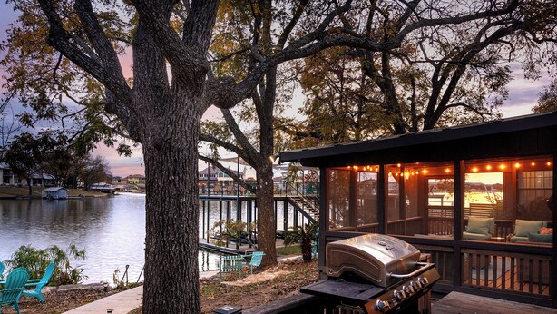 Terraza junto al lago con una parrilla, sillas y vistas al agua.